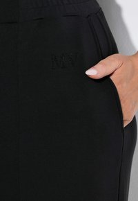 Zwarte broek van zacht materiaal met een zijzak. Heeft subtiele "MV" borduursel nabij de zak voor extra detail.
