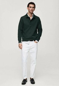 Dark green pullover with a collar, white button-down shirt underneath, paired with white trousers and black loafers. Simple, modern design.