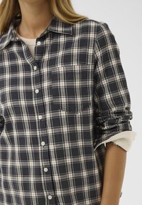 Camicia scozzese in cotone navy e crema con chiusura a bottoni, taschino sul petto singolo e maniche arrotolate. Caratterizzata da dettagli con bottoni bianchi.