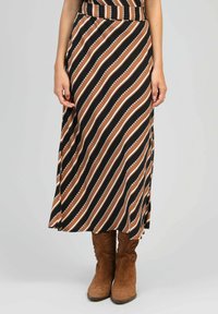 Jupe maxi avec de larges rayures diagonales en marron, noir et blanc. Tissu doux avec une taille ajustée et une fente sur le côté. Bottes de cow-boy marron.