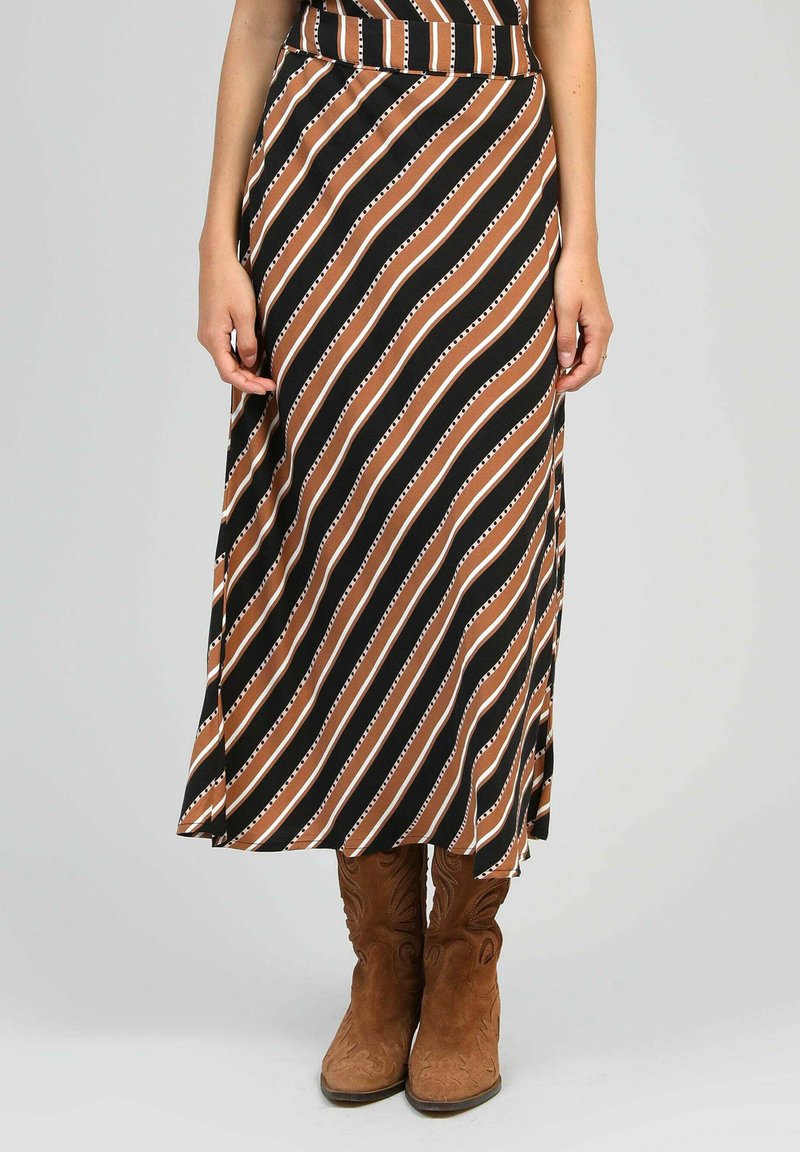 Jupe maxi avec de larges rayures diagonales en marron, noir et blanc. Tissu doux avec une taille ajustée et une fente sur le côté. Bottes de cow-boy marron.