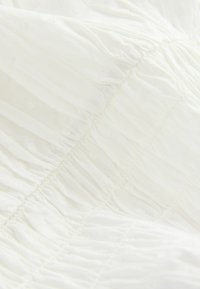 Tissu blanc texturé avec des plis froncés et de subtils points en relief, présentant un design doux et léger.