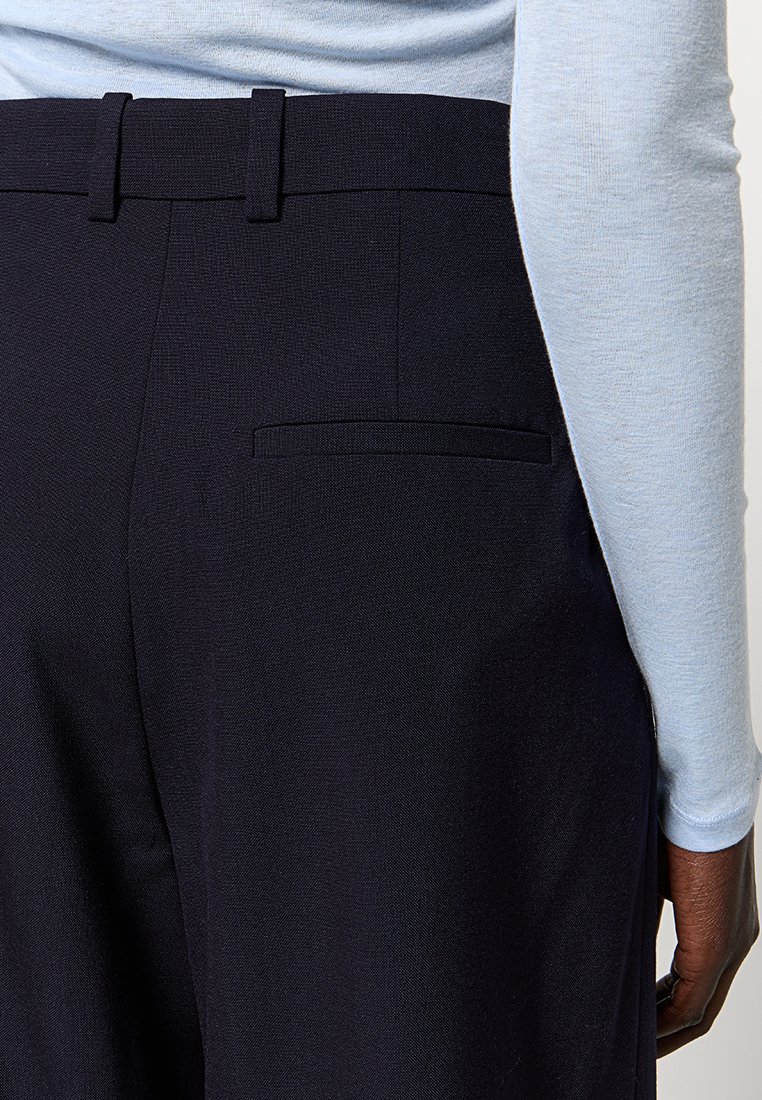 Granatowe spodnie o dopasowanym kroju z teksturowanym wykończeniem, z prostymi nogawkami, szlufkami na pasek i jedną tylną kieszenią, w zestawie z jasnoniebieską bluzką z długim rękawem.