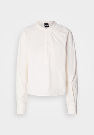 Witte blouse met lange mouwen, een ronde kraag en knoopsluiting, met subtiele verticale strepen, weergegeven op een effen achtergrond.