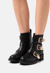 Czarne botki za kostkę wykonane z gładkiej skóry z trzema regulowanymi paskami na klamry i zamek błyskawiczny z boku. Masywna obcas z teksturowaną podeszwą.