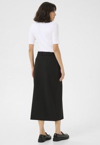 Jupe midi noire avec une texture lisse et une coupe ajustée. Associée à un top blanc ajusté et des chaussures noires brillantes.