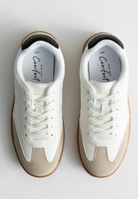 Vita sneakers med en slät läderöverdel, beige accenter och en texturerad gummisula. Har sex par snörhål och platta skosnören.