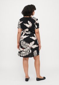 Short black dress with short sleeves, featuring a white and beige leaf pattern, cinched waist, and a flared skirt. Worn with black flats.