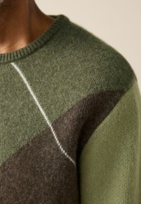 Knit sweater featuring a green and brown color block design with a round neckline, subtle texture, and contrasting white stitching.