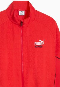 Veste rouge avec un motif géométrique texturé, col montant, fermeture éclair complète, et marquage Puma blanc avec logo sur le devant.