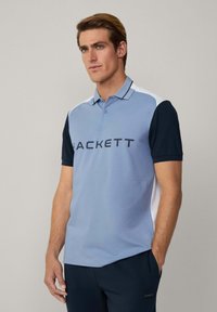 Polo shirt di colore azzurro chiaro con maniche blu scuro e dettagli bianchi. Presenta un colletto, tre bottoni e la scritta "HACKETT" stampata sul davanti.