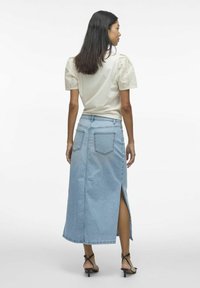 Gonna di jeans azzurro chiaro con uno spacco alto, abbinata a una blusa crema con maniche a sbuffo in broderie anglaise. Abbinata a tacchi neri con cinturini.
