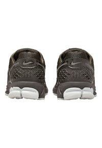 Nike-skor med en mörkbrun mesh-ovandel, triangulärt mönster på hälen, samt vit och grå gummisula. Diskret branding på hälen.