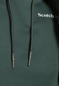 Groene hoodie met trekkingkoord en grijzige uiteinden. Voorzien van het witte "Scotch &" logo. Getextureerde katoenen stof met een gladde afwerking.