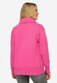 Pullover in pile di colore rosa brillante, con colletto alto, maniche lunghe e orlo a coste. Texture morbida con vestibilità comoda.