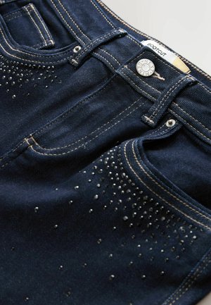 Bootcut denim jeans i mørkeblå med en glat tekstur. Har sølvfarvede nitter arrangeret i et gradientmønster langs fronten.