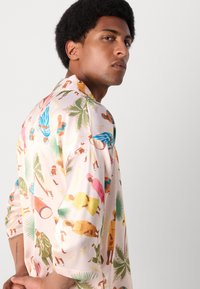 Camisa de manga corta en tejido rosa claro con patrones ilustrados coloridos de personas y plantas, con una textura suave y un corte relajado.