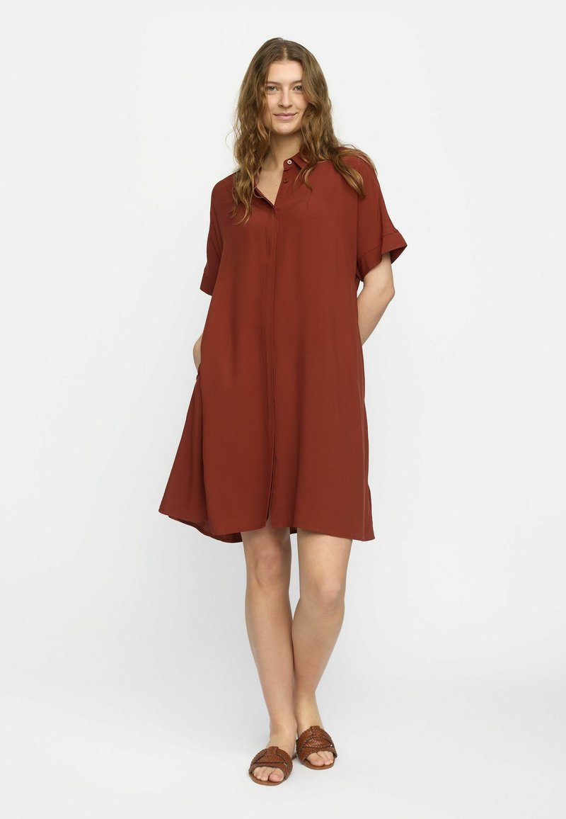 Rust-farbenes Hemdkleid mit Knopfleiste, kurzen Ärmeln und Seiten Taschen. Hergestellt aus glattem Stoff, hat es eine lockere Passform und einen knielangen Saum.