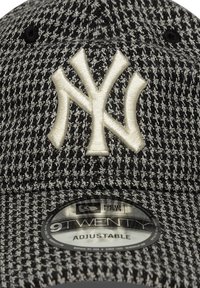 Casquette à damier noir et blanc avec une sangle ajustable, présentant un logo en relief de couleur crème des New York Yankees à l'avant et un autocollant de logo en dessous.