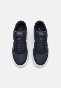 Granatowe sneakersy z elementami skórzanymi i zamszowymi, biała podeszwa środkowa, teksturowane sznurowadła oraz logo Tommy Hilfigera na języku.