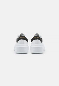 Adidași albi cu partea superioară din piele netedă, accente negre din întoarsă la călcâi și o talpă din cauciuc albă. Logo-ul de marcă de culoare aurie pe spate.