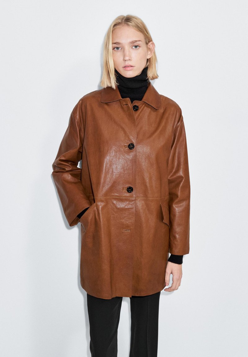 Brun læderjakke med krave, sorte knapper og to sidelommer. Har en afslappet pasform og glat tekstur.