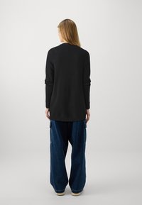 Svart stickad tröja med långa ärmar och ribbad fåll, matchad med lösa blå denimbyxor som har sidfickor och en avslappnad passform.