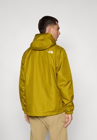 Veste imperméable jaune avec capuchon, dotée de poignet élastiques et d'un logo sur le haut du dos. Texture lisse, coupe décontractée et ourlet droit.