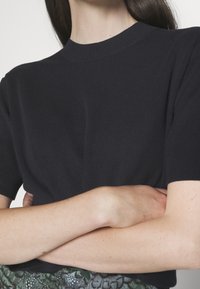 Granatowy, prążkowany, dzianinowy top z krótkim rękawem i wysokim dekoltem. Tekstura materiału jest gładka, przylegająca do ciała, bez widocznych wzorów.