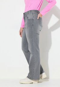 Jeans in denim grigio con una vestibilità rilassata, caratterizzati da una vita cucita e tasche. Il modello indossa una maglia a maniche lunghe rosa e scarpe bianche.