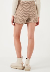 Hnedé a krémové houndstooth šortky s textúrovaným povrchom, spárované s béžovými členkovými čižmami s masívnou podrážkou a dekoratívnymi akcentmi.