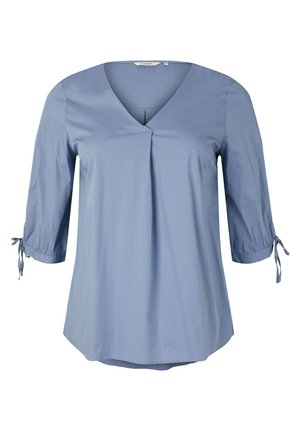 Blusa azul claro con mangas tres cuartos, escote en V, pliegue frontal y pequeños lazos en los puños de las mangas.