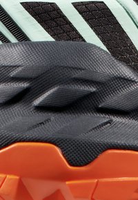 Scarpa da corsa con una tomaia nera testurizzata e strisce di accento verde menta, e una suola nera con pattern e un battistrada arancione per la presa.