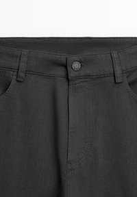 I pantaloni in denim neri presentano una vita piatta, passanti per la cintura e una chiusura con bottone. La texture è liscia, con cuciture sottili e tasche laterali.