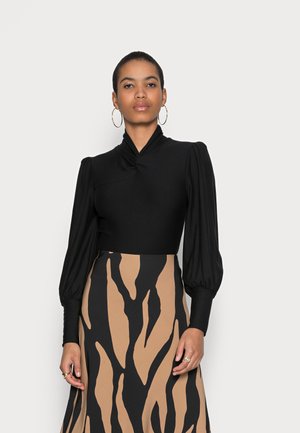 Bodysuit noir avec un col haut et des manches bouffantes, associé à une jupe à motifs avec de larges rayures noires et beiges.