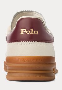 Deportiva blanca con talón de cuero burdeos, marca "Polo" en dorado y suela de goma marrón. Parte superior de ante con detalles cosidos.