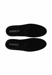 Chaussures en suède noir au design épuré, avec un bout rond, un laçage subtil et une surface texturée. Le branding est visible sur la semelle intérieure.