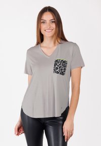 Camiseta gris de cuello en V con mangas cortas, que presenta un bolsillo negro con estampado de leopardo bordeado en verde neón. Tejido suave, corte relajado y bajo curvado.