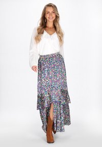 Lila és zöld paisley mintás maxi szoknya, réteges fodros designnal, oldalsó hasítékkal. Fehér blúzzal és barna csizmával viselve.