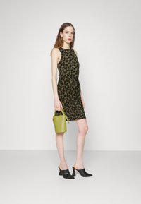 Vestido preto com padrão floral amarelo, design ajustado, até ao joelho. Complementado com uma pequena bolsa verde e sapatos de salto abertos pretos com franjas.