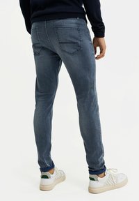 Jeans de mezclilla azul descoloridos con corte slim, que cuentan con dos bolsillos traseros y una cinturilla acanalada, combinados con zapatillas blancas.