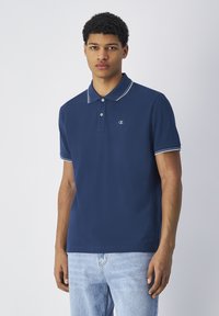 Granatowa koszulka polo z białym kołnierzykiem i akcentami na rękawach, wykonana z bawełny, z małym logo po lewej stronie klatki piersiowej, krótkie rękawy.
