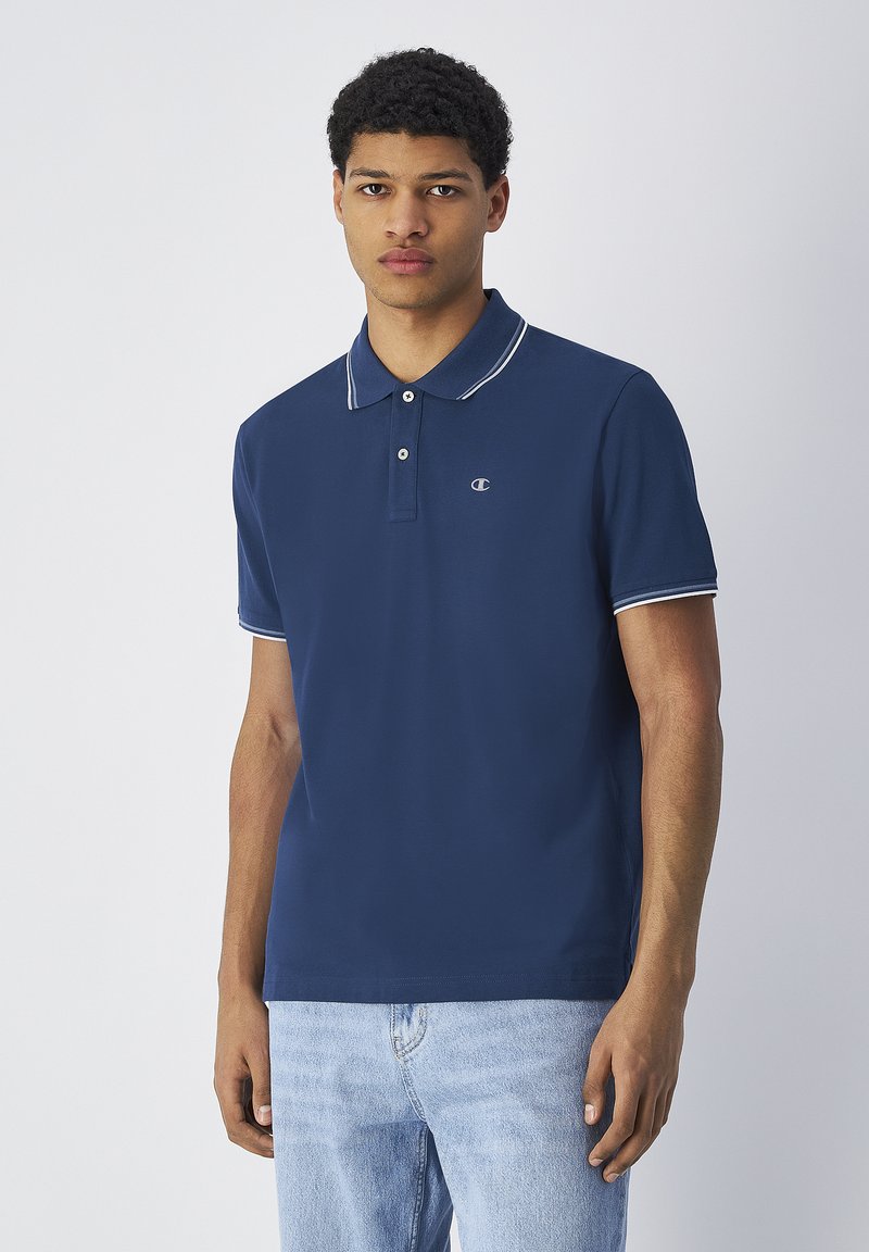 Granatowa koszulka polo z białym kołnierzykiem i akcentami na rękawach, wykonana z bawełny, z małym logo po lewej stronie klatki piersiowej, krótkie rękawy.