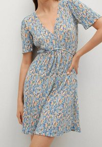 Blaues Blumenkleid mit kurzen Ärmeln, V-Ausschnitt und taillierter Taille. Hergestellt aus leichter Stoffqualität mit orangefarbenen, weißen und grünen Blumenmustern.