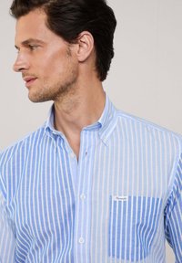Camicia button-up a righe blu chiaro con taschino e accentatura blu uniforme. Realizzata in un tessuto leggero e testurizzato.