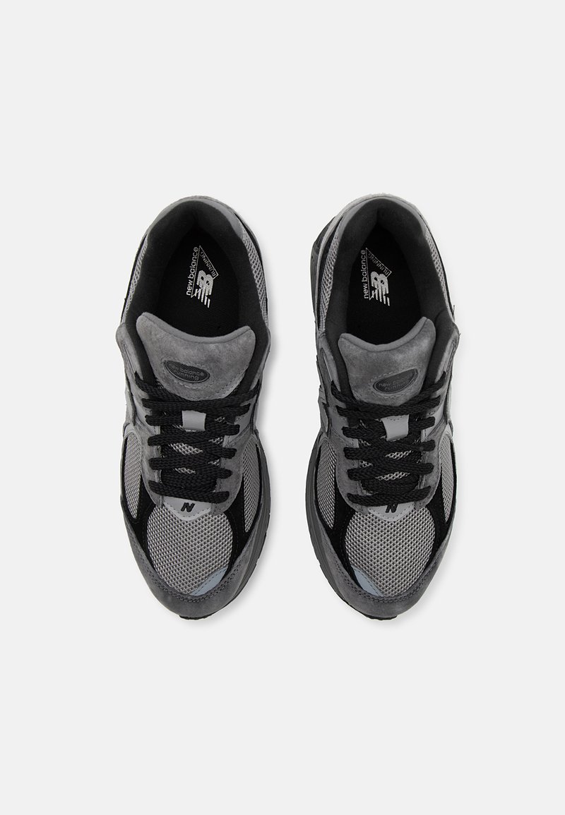 Baskets de sport grises avec une tige en mesh, des accents en daim et des lacets noirs. Des détails réfléchissants et une semelle extérieure rembourrée sont visibles.