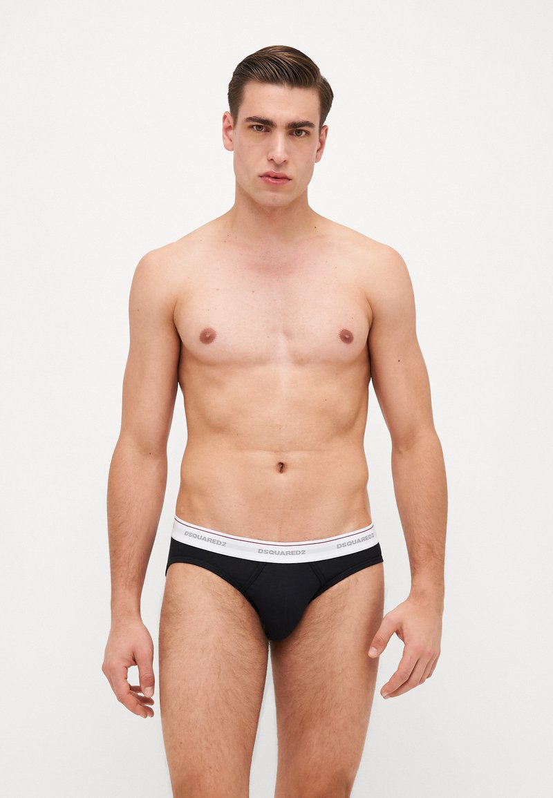 Culottes pour hommes en tissu noir avec une ceinture élastique blanche portant le nom de la marque imprimé. Le design est ajusté avec une couverture minimale et des coutures.