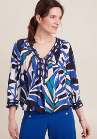 Bluse mit V-Ausschnitt, mit einem blauen und weißen Blattmuster, aus leichtem Stoff; Dreiviertelärmel mit geknöpften Manschetten.
