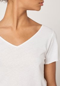 Valge V-kaelusega T-särk, valmistatud kergest kangast; sisaldab lühikesi varrukaid ja lõdvestunud lõiget. Kaelus ja alläär on peene õmblusega.