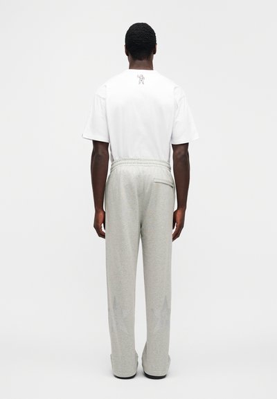 Λευκό κοντομάνικο μπλουζάκι με μικρό γραφικό στο πίσω μέρος, συνδυασμένο με ανοιχτό γ κρι παντελόνι φόρμας με σχέδια αστεριών. Ελαστική μέση.